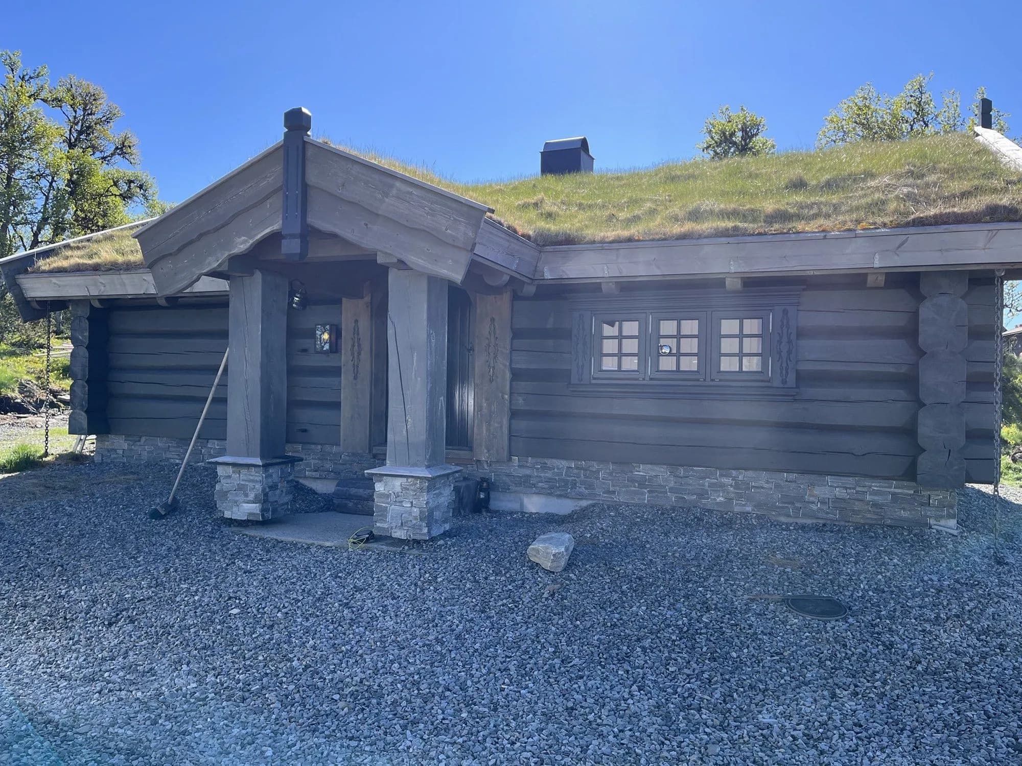 Anneksset med inngangsparti og søyler på steinsokler, torvtak og grånet tømmer, om sommeren.