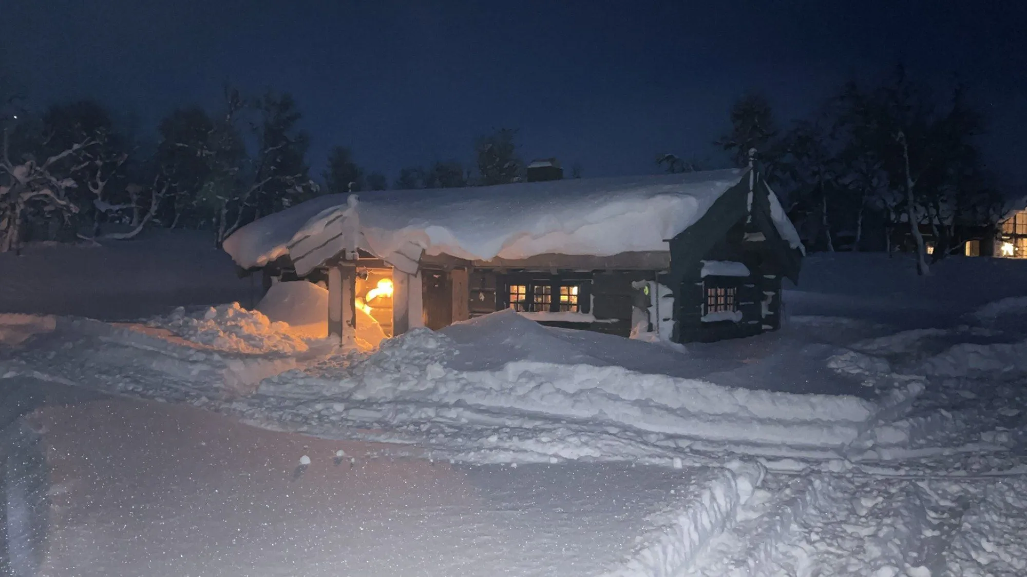 Det snødekte anneksset i skumringen, med lys som lyser opp i vinterlandskapet.