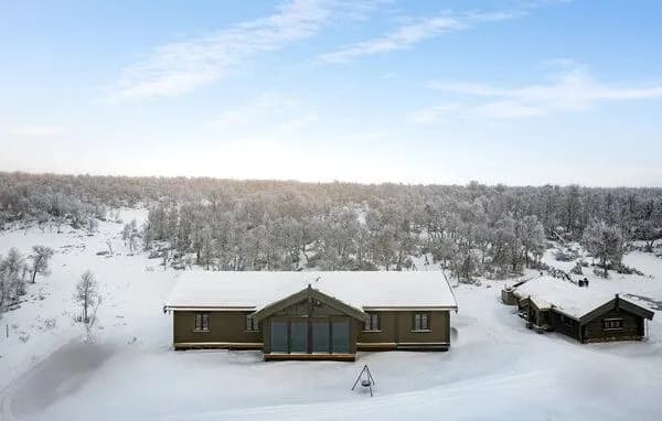Hytta sett forfra om vinteren, med nabohytter og snødekt fjellterreng i bakgrunnen.